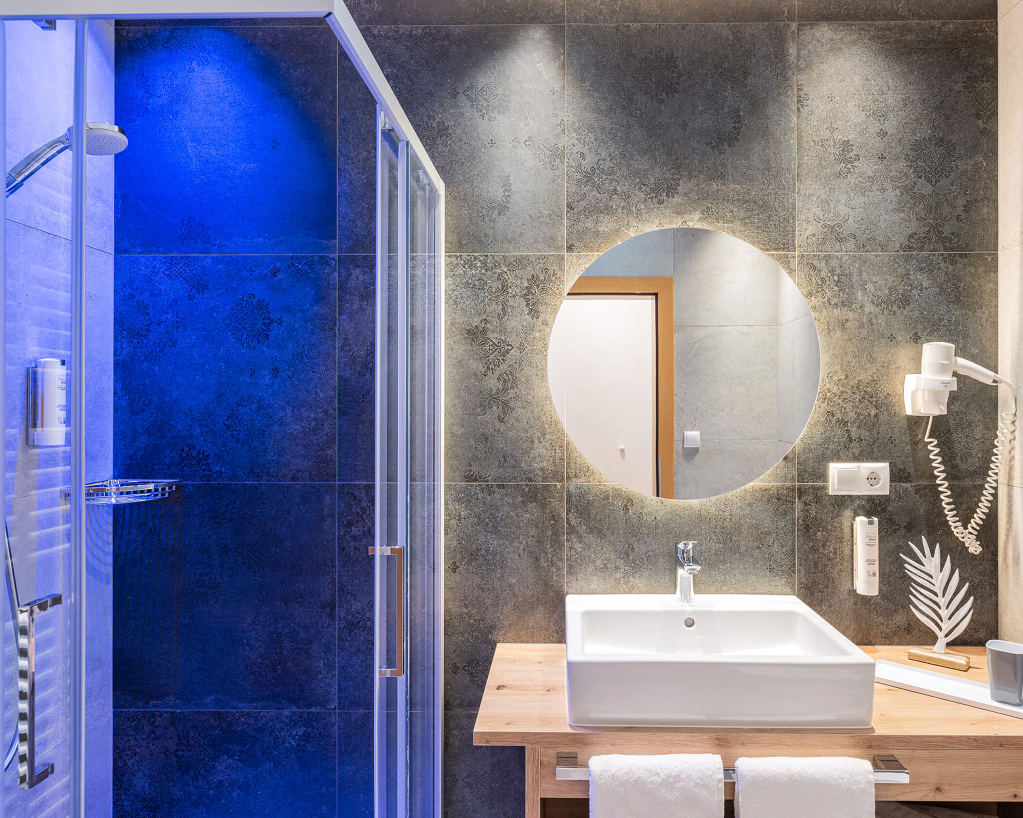 Badezimmer mit beleuchteter Dusche, Waschbecken und rundem Spiegel im Apartment Typ B - Hotel Anewandter