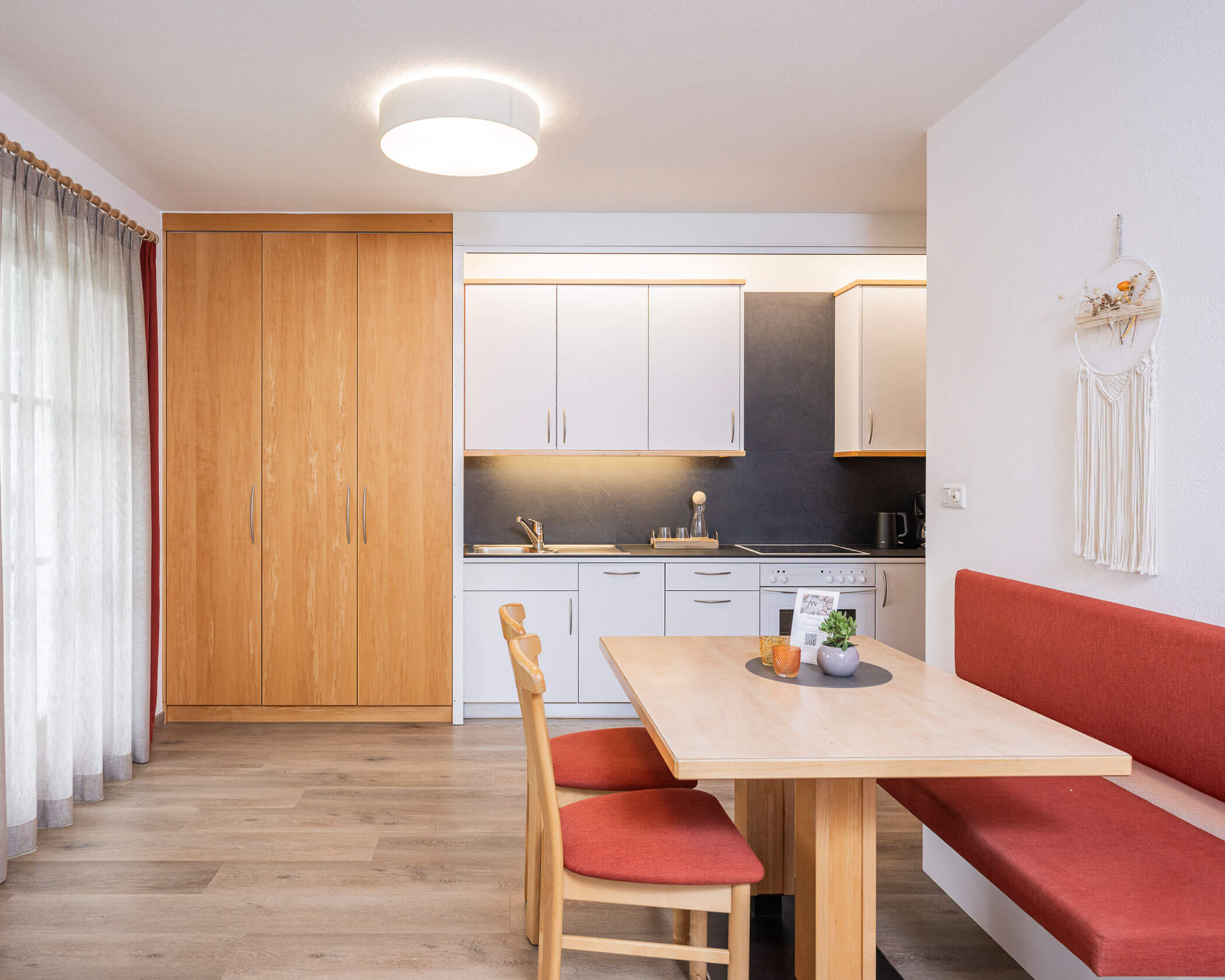 Weiße Küche mit Holzschrank daneben und Esstisch davor im Apartment Typ C - Hotel Anewandter