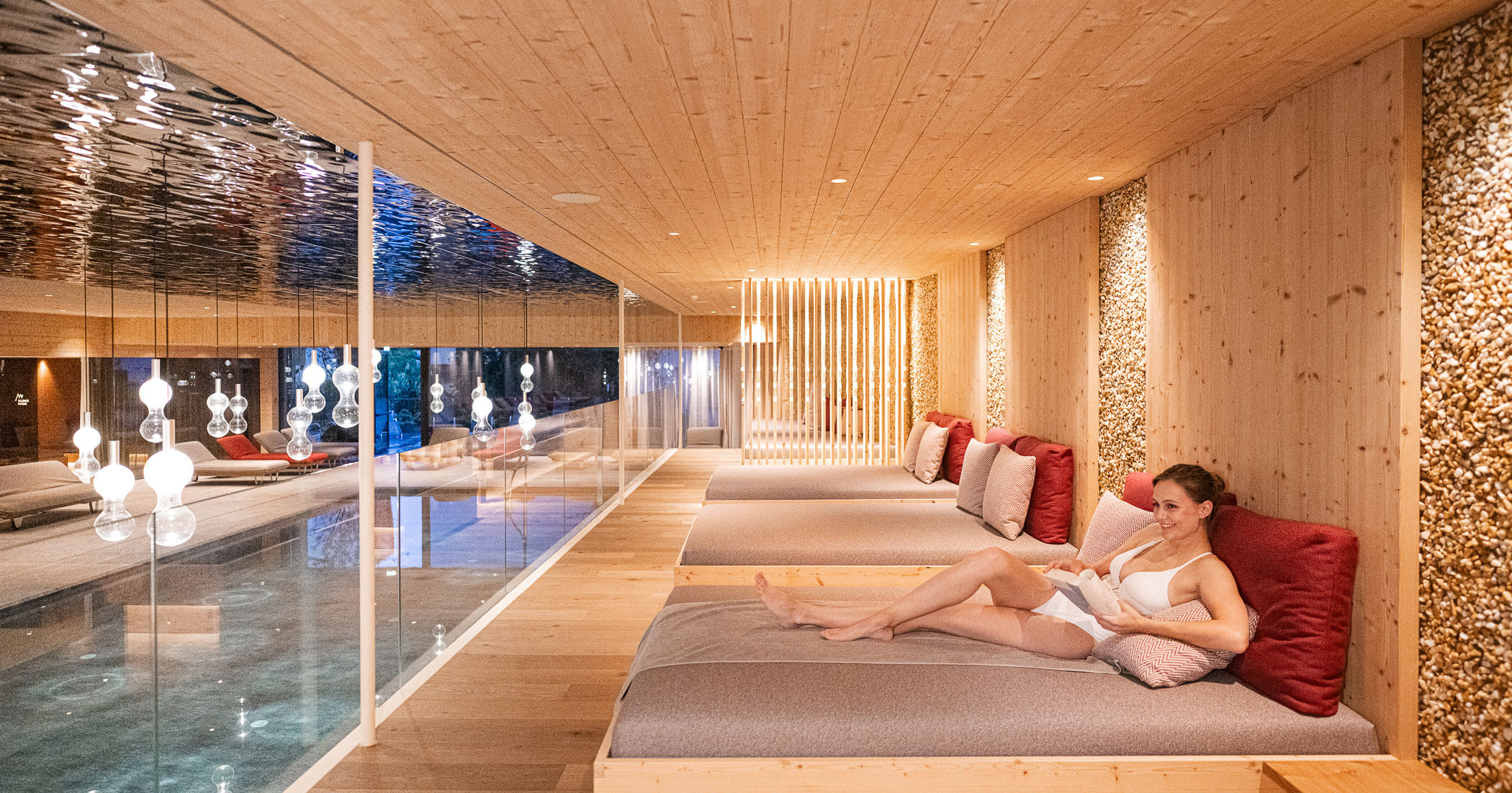 Donna sdraiata su un lettino davanti alla piscina interna nell'area benessere - Hotel Anewandter