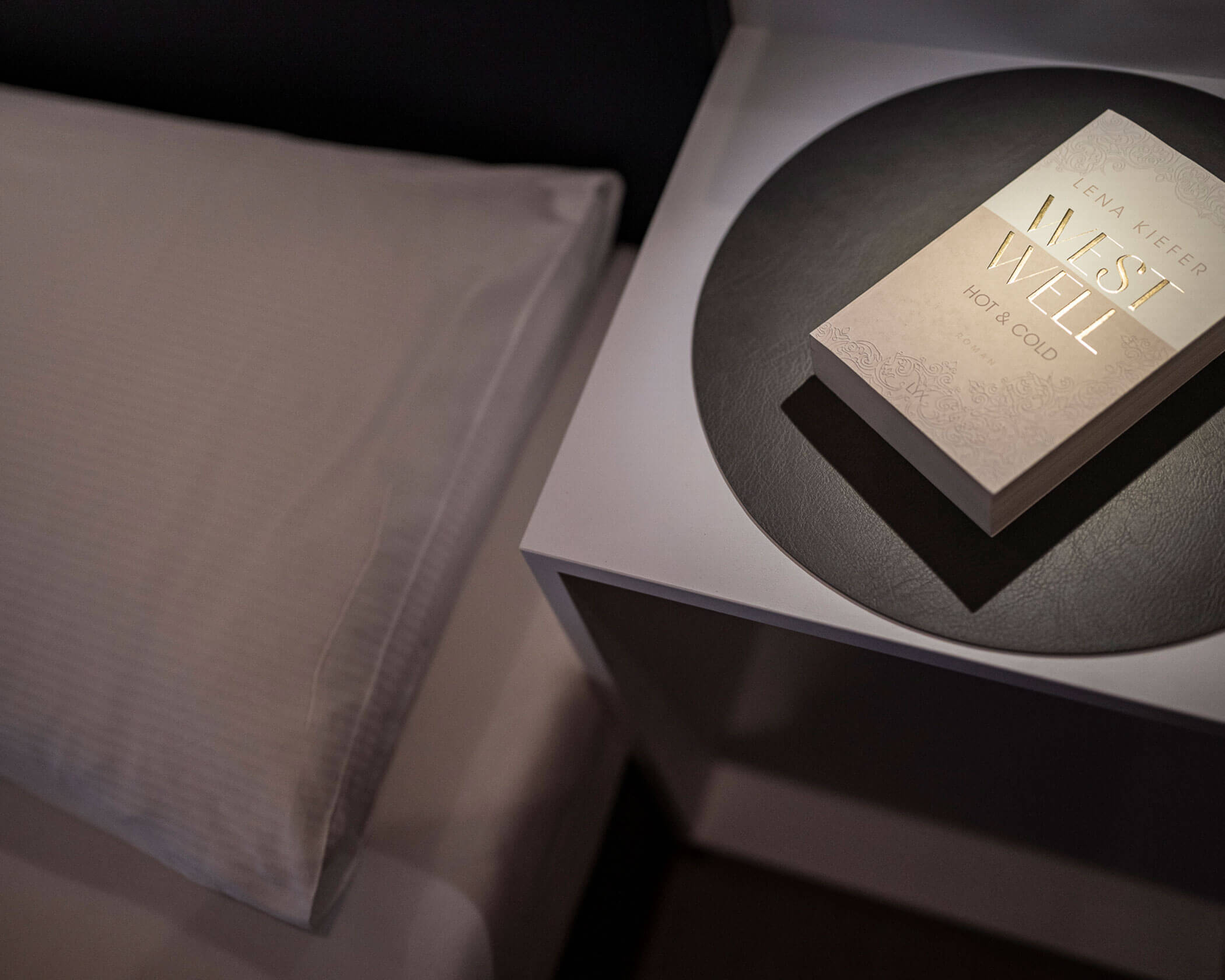 Nachttisch mit einem Buch darauf und daneben ein Bett - Hotel Anewandter