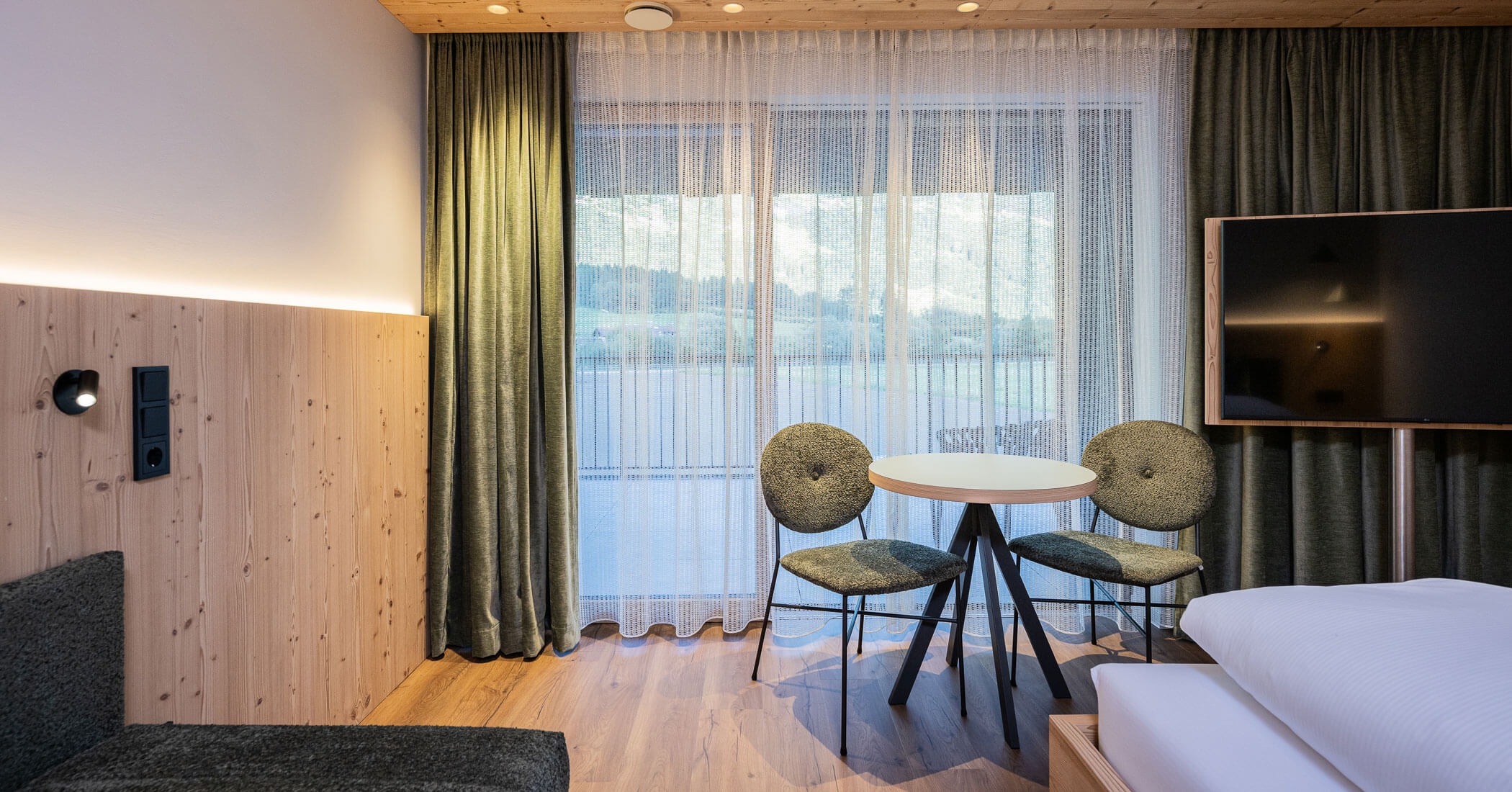 Camera da letto con televisore, sedie e tavolo rotondo - Hotel Anewandter