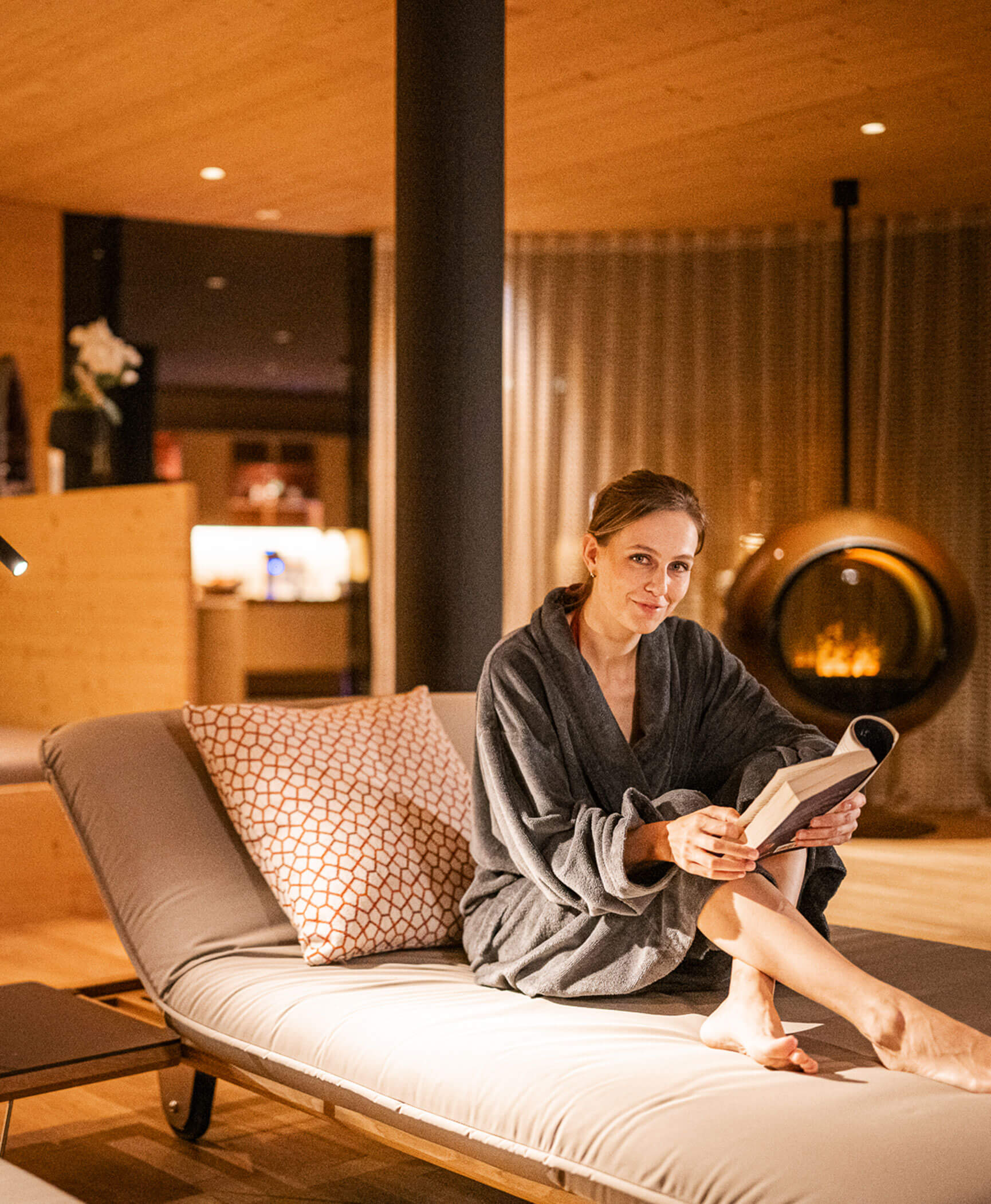 Woman sitting with a book on a lounger in the wellness area - Hotel Anewandter