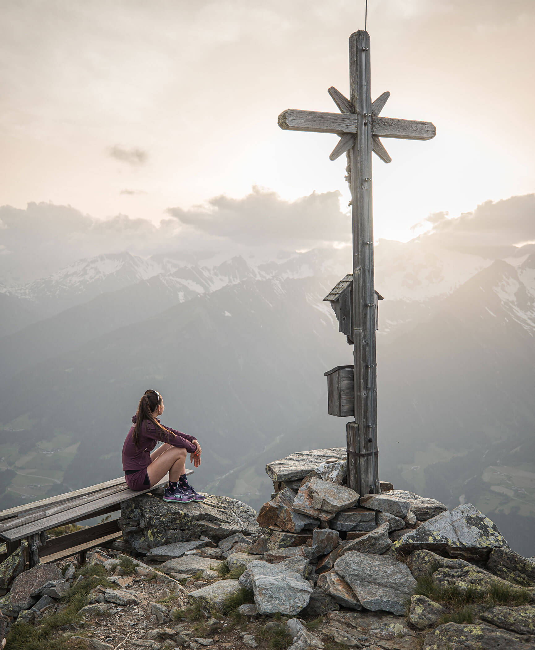 Eine Frau sitzt auf einer Bank vor einem Gipfelkreuz - Hotel Anewandter